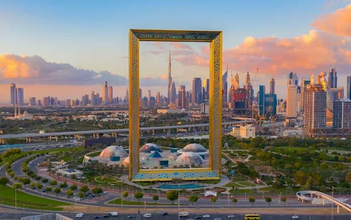 The golden Dubai Frame with the Downtown skyline and Zabeel Park behind it at sunset