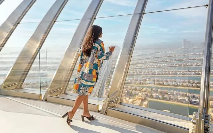 A woman looking out over Palm Jumeirah through the curved glass of The View at The Palm