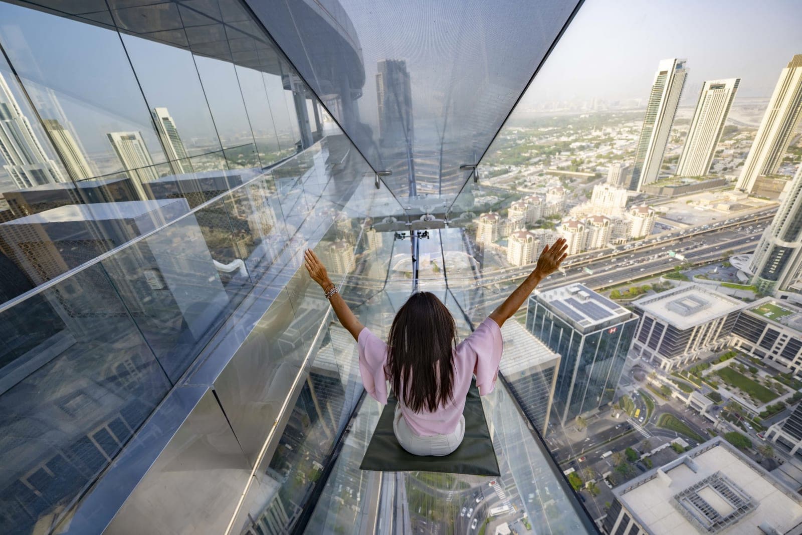 A visitor sitting on the glass floor of Sky Views Observatory above the Dubai skyline
