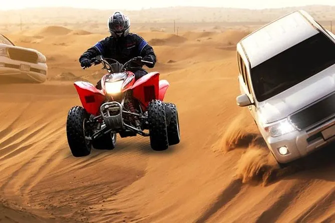A rider on a red quad bike crossing the dunes beside a four wheel drive