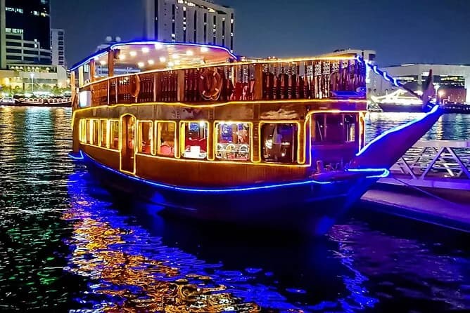 A two deck dhow outlined in lights on Dubai Creek at night