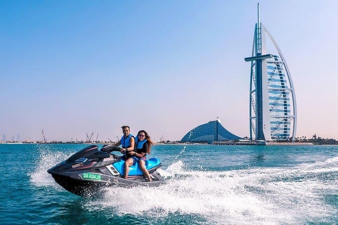 Two riders on a jet ski on the water with the Burj Al Arab behind them